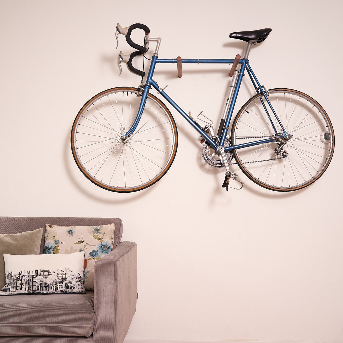 Blue bicycle mounted with poles on a white wall above a sofa.