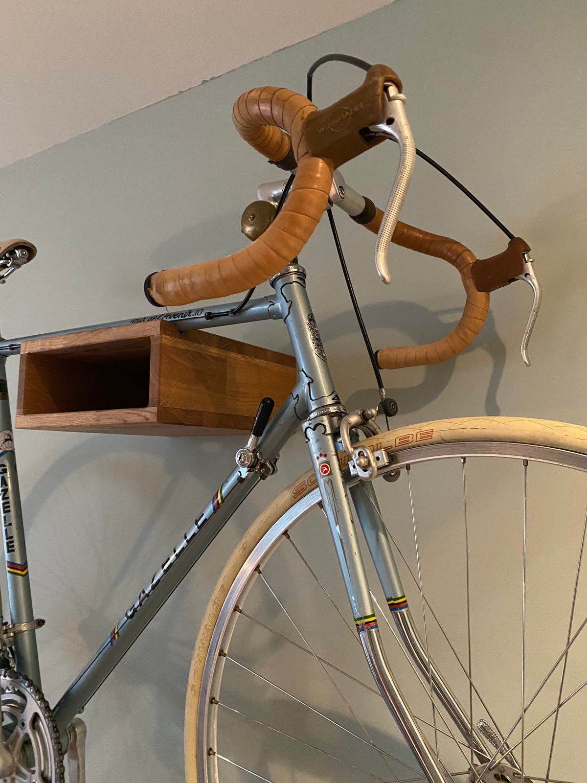 A close-up of a vintage-style bicycle hanging on an oak bike hanger on the wall.